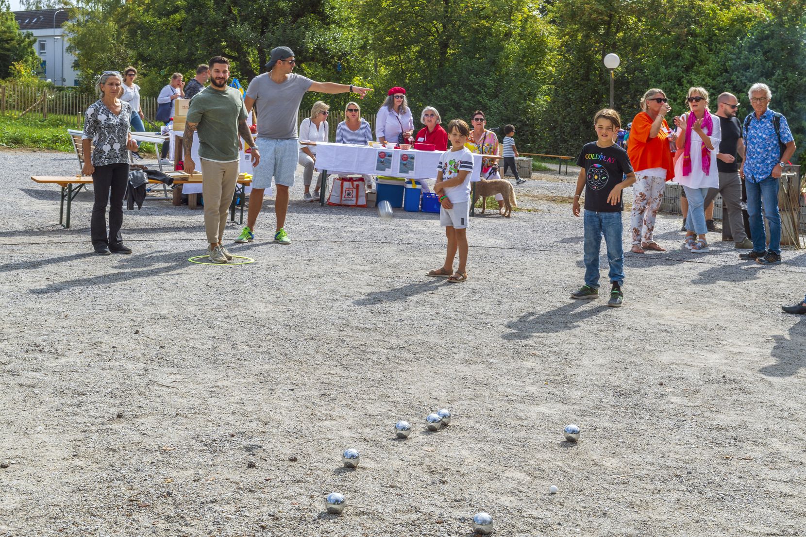 Menschen stehen auf einem Kiesplatz und spielen Boule.